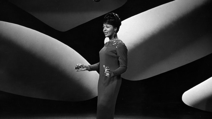 Eleanor Collins en 1966 debout sur une scène portant une robe longue.