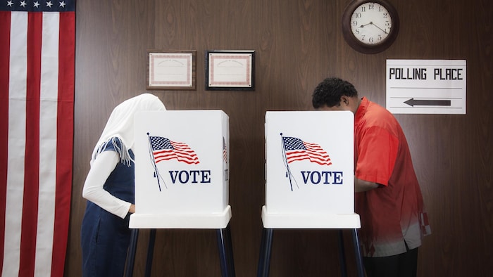 Une électrice et un électeur, chacun derrière un panneau dans un bureau de vote aux États-Unis.