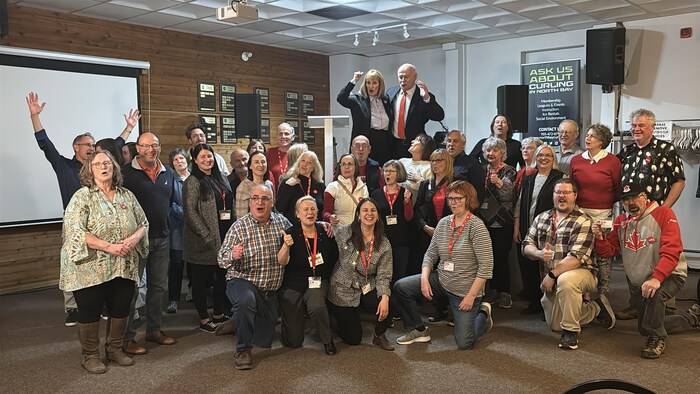 Des personnes en joie dans une salle lèvent les mains. 