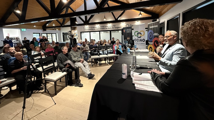 Vue sur le public, parsemé dans la salle, et sur les candidats au débat.