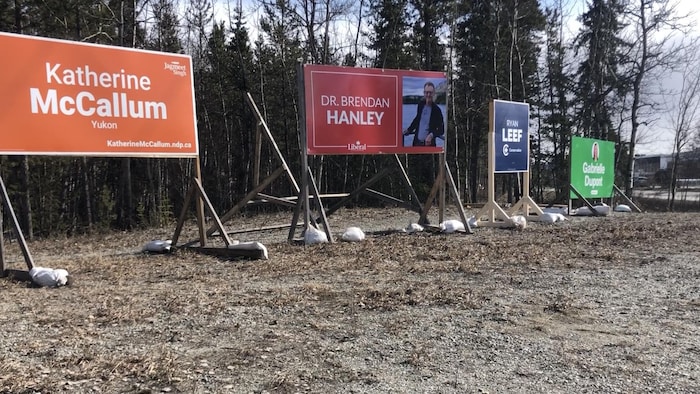 Quatre grandes pancartes sur le bord d'une rue au soleil, le 12 avril.