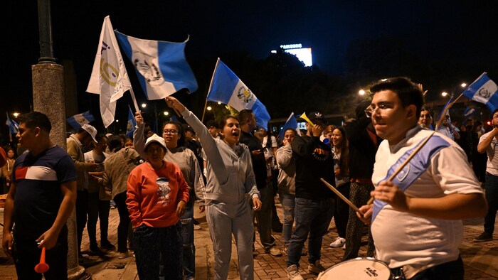 Des partisans, drapeaux du Guatemala en main, défilent dans la rue.
