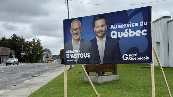 Une pancarte électorale du Parti québécois, montrant les photos de Sébastien D'Astous et de Paul St-Pierre Plamondon. En arrière-plan, la cathédrale d'Amos.