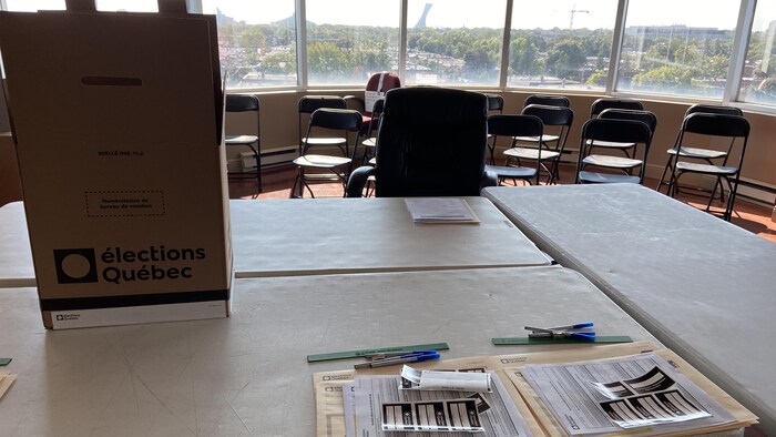 Une urne électorale sur un bureau avec des chaises vides.