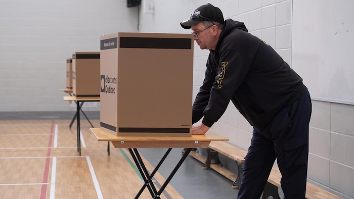 Un homme portant une casquette se penche au-dessus d'un isoloir en carton dans un bureau de vote.
