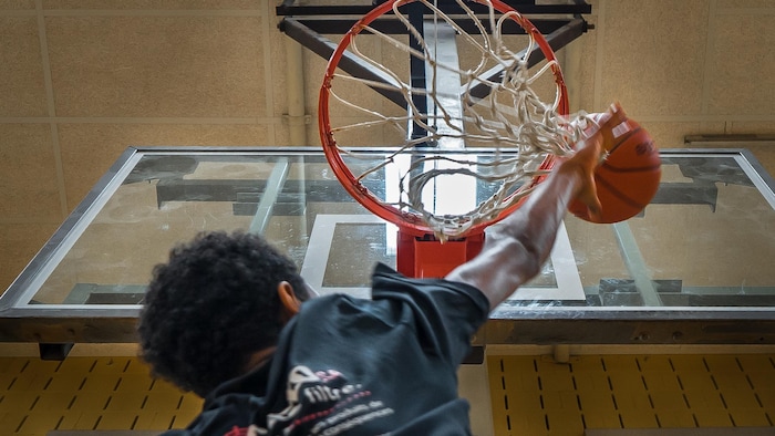 Un jeune lance un ballon vers un panier de basketball.