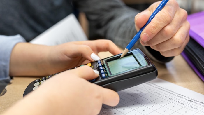 Une élève tient une calculatrice dans ses mains près d'un enseignant.