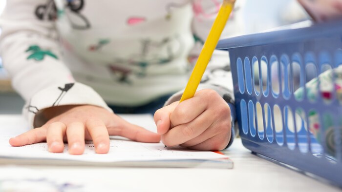 Une élève qui écrit sur une feuille avec un crayon.