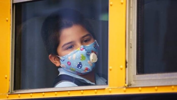 Un élève portant un masque regarde par la fenêtre de l'autobus scolaire dans lequel il est assis.
