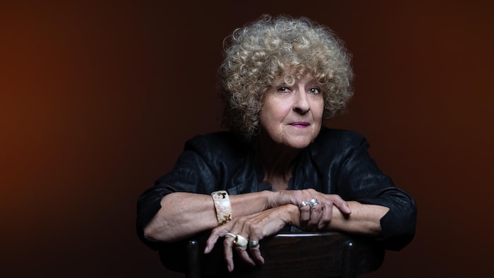 Portrait de l'autrice, assise sur une chaise retournée, les bras croisés. 
