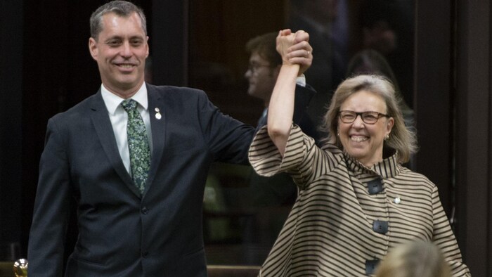 Elizabeth May et Paul Manly se tiennent la main en l'air en souriant.