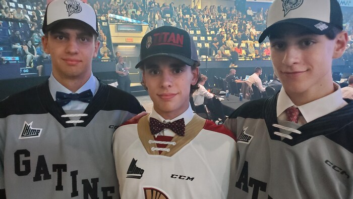 Trois jeunes joueurs de hockey dans un amphithéâtre.