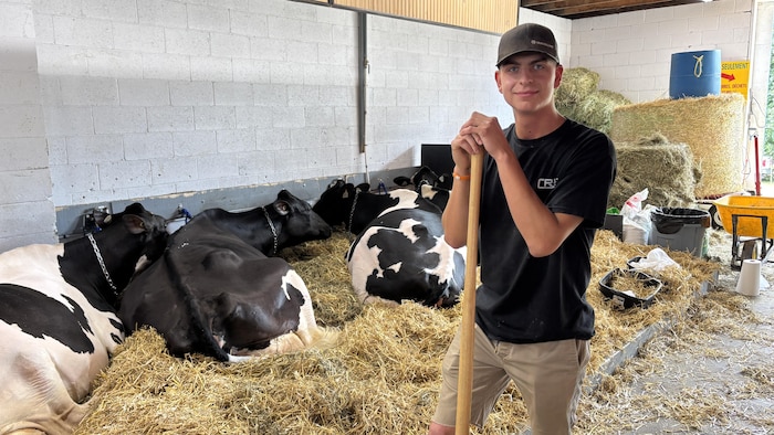 Éloi Hudon tient un outil de ferme devant ses vaches.