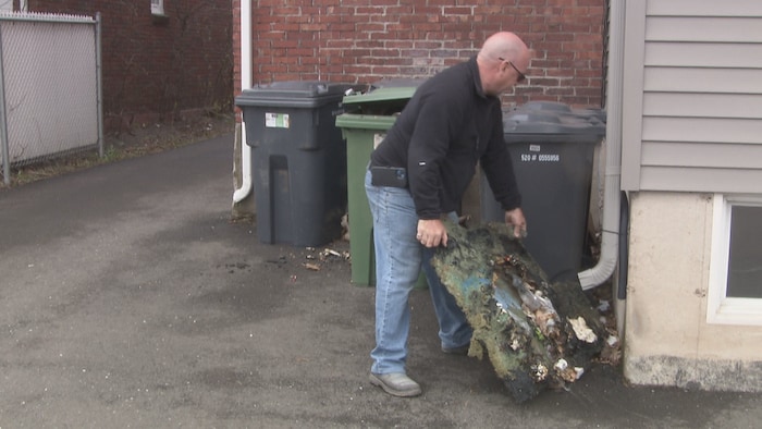 Un homme près des poubelles transporte une poubelle ravagée par le feu. 