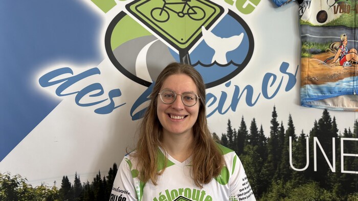 Éloïse Carré pose devant le logo de la Corporation de la Véloroute des baleines.
