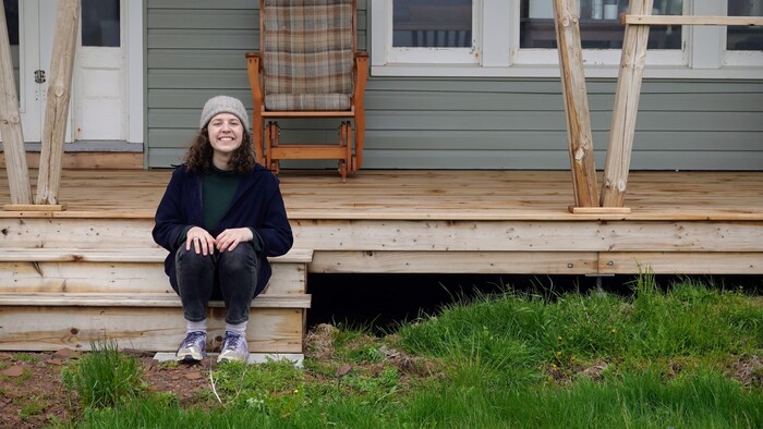 Une jeune femme assise sur les marches en bois de l'entrée d'une maison de campagne.