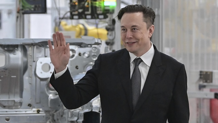 Elon Musk salue de la main dans une usine de Tesla.