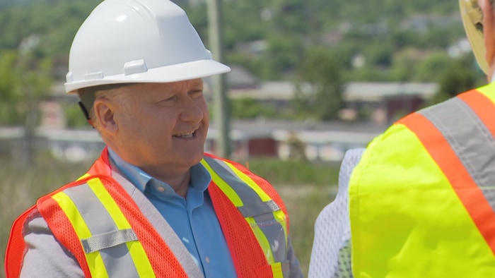 Le ministre porte un casque de chantier et une veste réfléchissante.