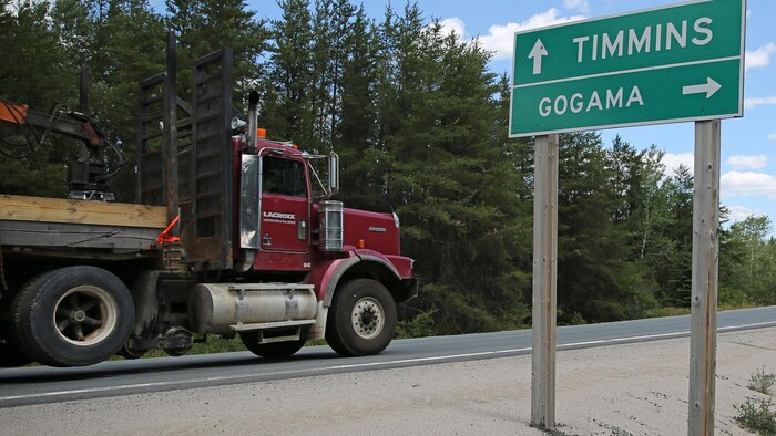 Le panneau au bord de la route indique les directions vers Timmins et Gogama. Un camion passe sur la route en arrière-plan.