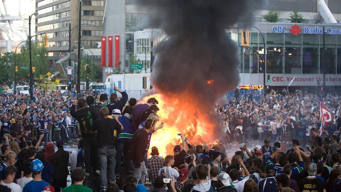 Une foule de partisans des Canucks de Vancouver regardent une voiture brûler lors des émeutes au centre-ville de Vancouver.