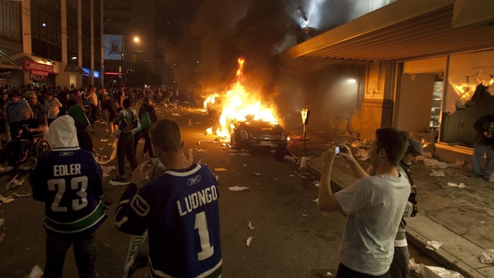Une foule est rassemblée sur la rue Georgia de Vancouver durant les émeutes de 2011, plusieurs voitures sont en train de brûler.