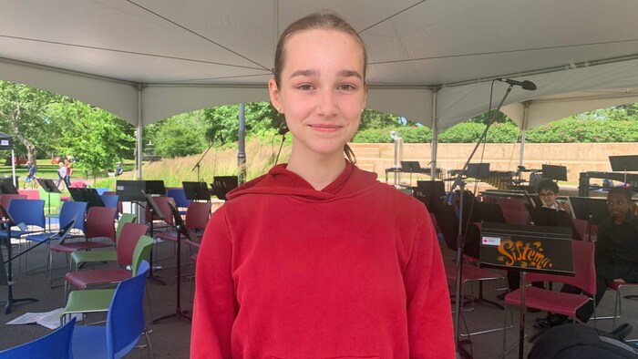 Une adolescente membre d'un orchestre debout sous un chapiteau. Elle regarde la caméra et sourit.