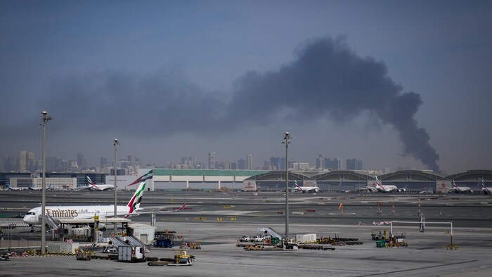 L'aéroport de Dubaï, le jour, avec une demi-douzaine d'appareils cloués au sol et une épaisse fumée noire à l'horizon.