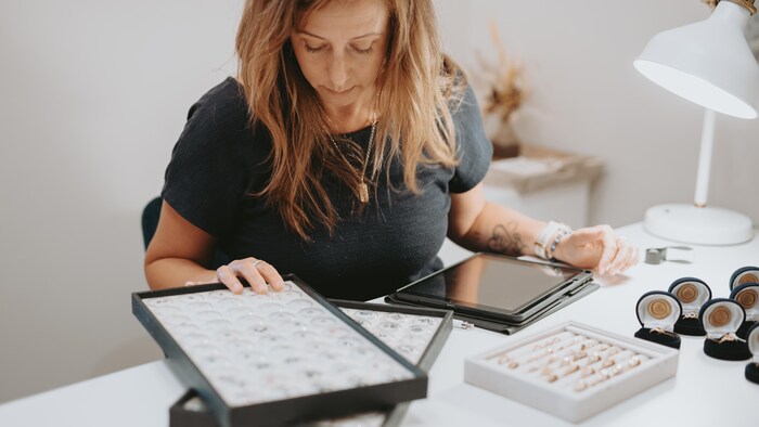 Une femme assise à un bureau devant des bagues et des bijoux en or.