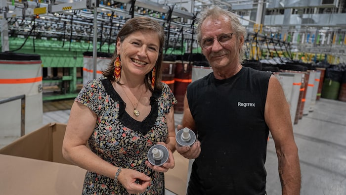 Une femme et un homme tiennent un outil en plastique dans une usine de textile.