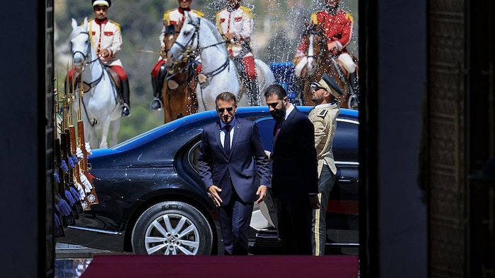 Emmanuel Macron, salué par un militaire, marche aux côtés d'Ahmed Al-Chara après être sorti d'une voiture, sous les yeux de quatre militaires à cheval en tenue d'apparat.