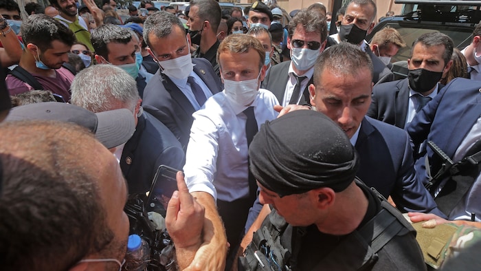 Emmanuel Macron, masqué, est entouré de gardiens de sécurité au milieu d'une foule dans une rue. 