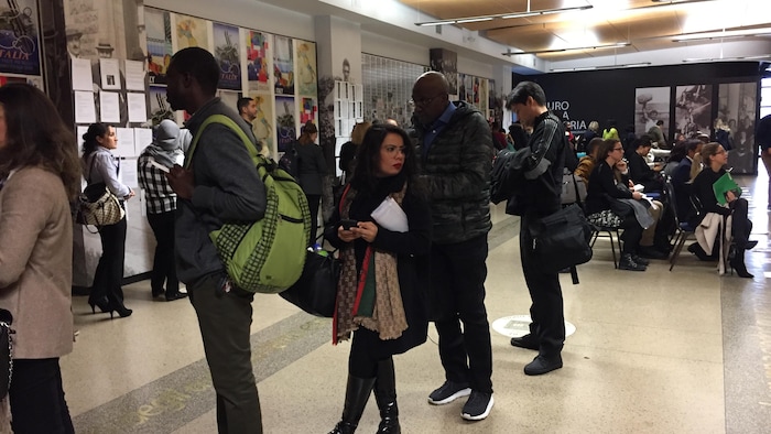 أشخاص من عرقيات مختلفة يقفون في طابور انتظار داخل مبنى.