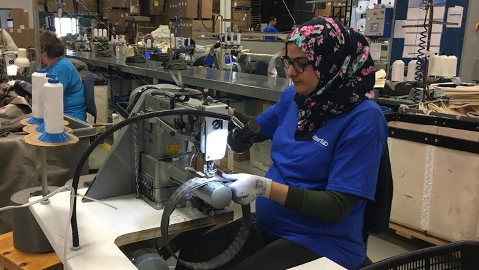 عاملة تضع حجاب رأس جالسة خلف ماكينة خياطة صناعية.