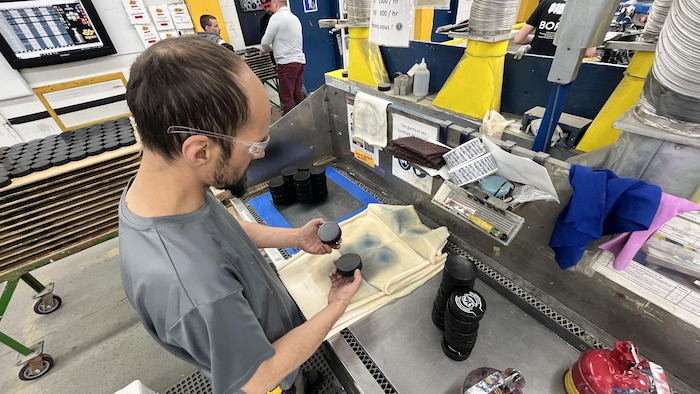 Un employé tient des rondelles dans ses mains, à une station de travail.