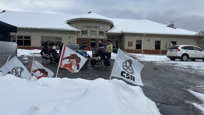 Des employés font le piquet de grève devant un CPE en hiver.