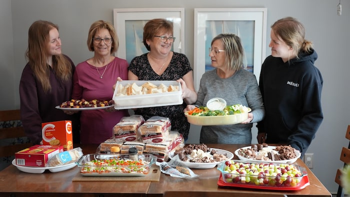Des personnes en train de montrer des récipients avec plein de nourriture et une table avec encore plus de plats préparés, à Fatima, aux Îles-de-la-Madeleine, en mars 2025.