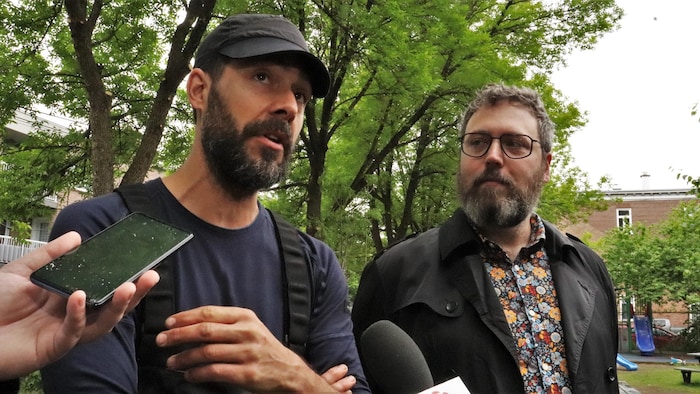 Deux hommes dans un parc s'adressent aux caméras.