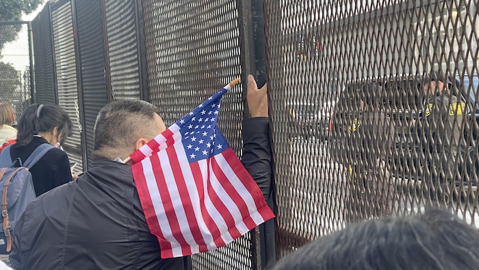 Une personne tenant un drapeau des États-Unis se tient à côté d'un haut grillage.