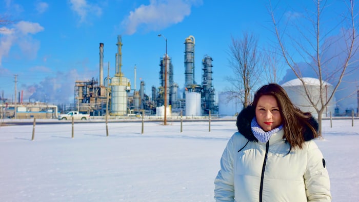 Janelle Nahmabin est devant une raffinerie qui se trouve en bordure de la réserve Aamjiwnaang.