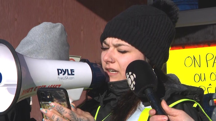 Une femme coiffée d'une tuque prononce une allocution en public dans un mégaphone.
