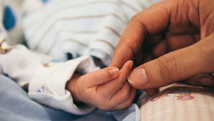 Une main de femme tient les doigts d'un bébé.