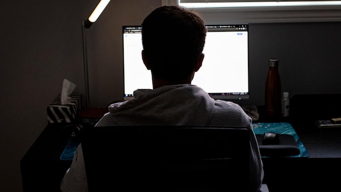 Un enfant suit son cours en ligne devant un écran d'ordinateur.