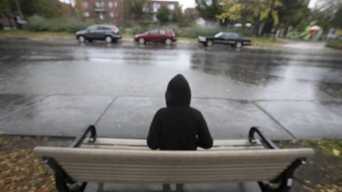 Un garçon est assis seul sur un banc au bord de la rue.