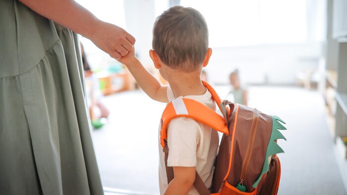 Un enfant avec un sac à dos tient la main de sa mère à son arrivée à la maternelle.