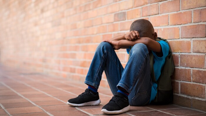 Un jeune garçon noir est assis au sol, visage caché.