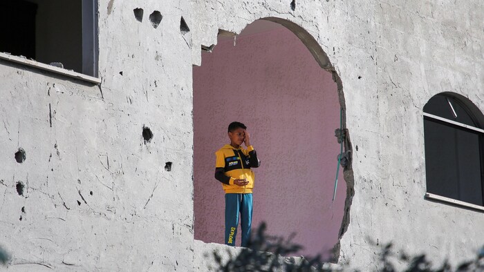 Un enfant debout dans un bâtiment endommagé par des frappes à Rafah. On l'aperçoit à travers un trou dans le béton.