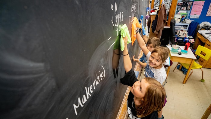 des enfants nettoient un tableau dans une classe.