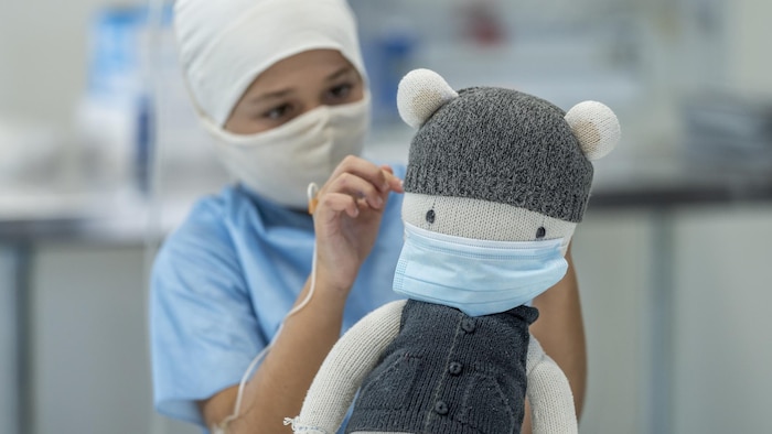 Un enfant de 9 ans assis dans un hôpital avec une intraveineuse, un masque et une casquette.
