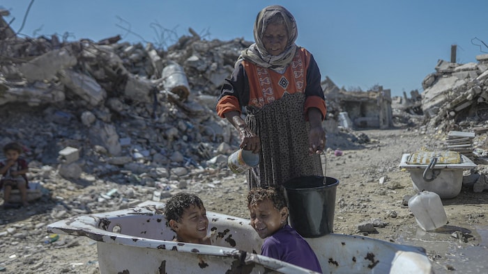 Une Palestinienne lave des enfants dans une baignoire au milieu des décombres, dans le quartier d'Al-Zarqa à Gaza, le 21 septembre 2026.