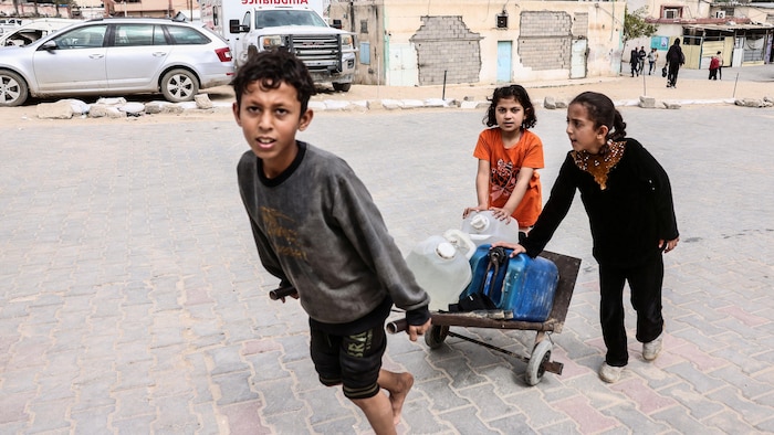 Un petit garçon et deux petites filles transportent des bidons d'eau. 